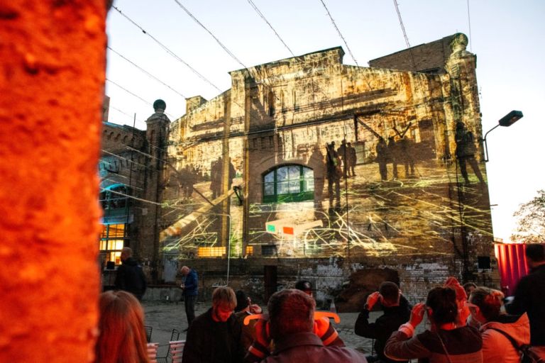 Einige Menschen schauen sich einen Film an, der im Freien an die Fassade einer alten Fabrik projeziert wird.