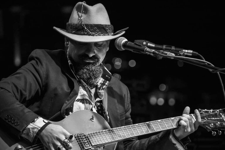 Schwarz-Weiß-Foto des Musikers mit Bart, Cowboyhut und Gitarre bei einem Auftritt