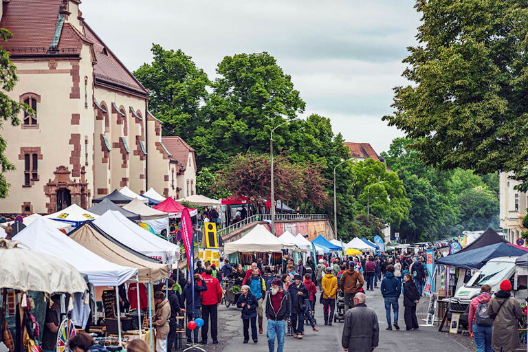 Auf einer Straße sind auf beiden Seiten Stände und Pavillons aufgebaut, zwischen denen viele Menschen unterwegs sind.