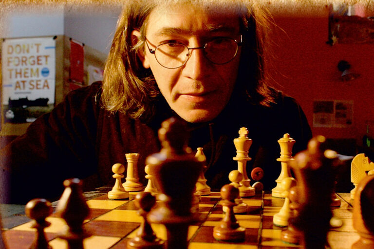 Daniel Schade schaut über ein Brett mit Schachfiguren ernst in die Kamera.