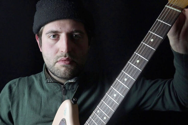 Foto des starr in die Kamera blickenden Musikers mit seiner Gitarre