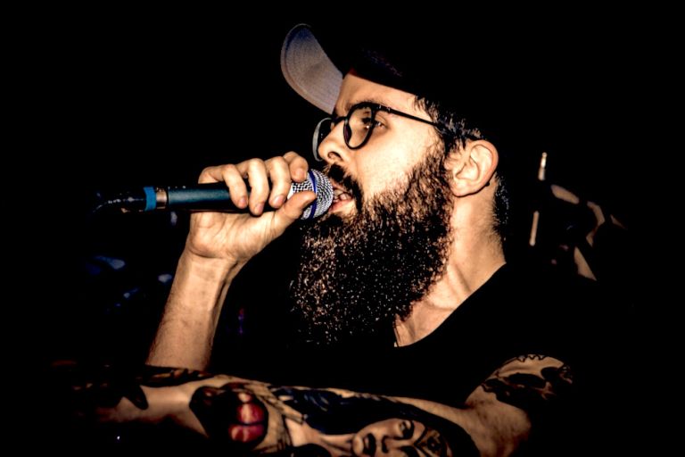 Der Rapper trägt bei einem Auftritt Vollbart, Brille und Basecap.