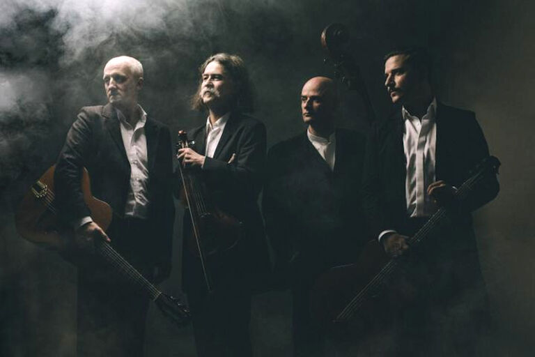 Düster wirkendes Gruppenfoto der Musiker mit ihren Instrumenten in einem dunklen Raum mit Nebel