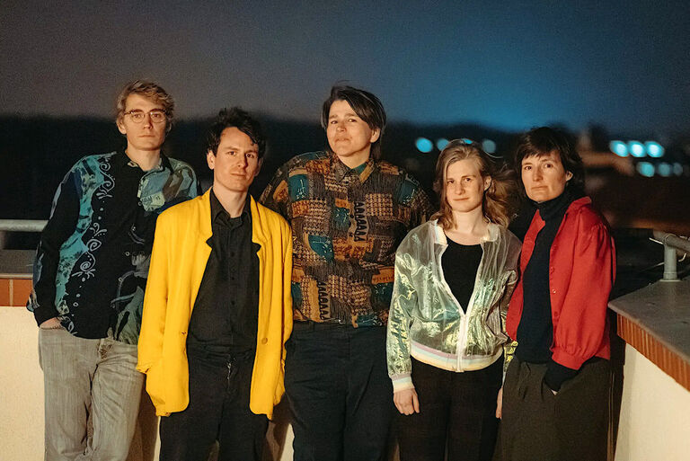 Gruppenbild der ernst blickenden Musikerinnen und Musiker bei Nacht auf einer Dachterrasse