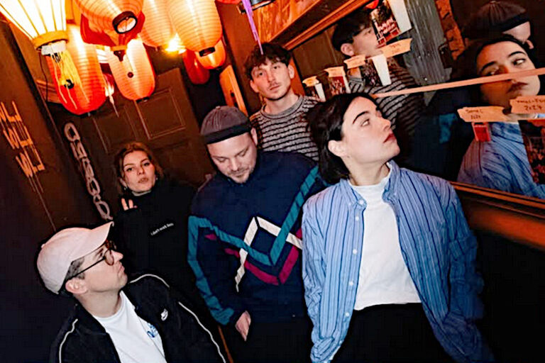 Foto der Band in einem kleinen Raum mit Spiegeln