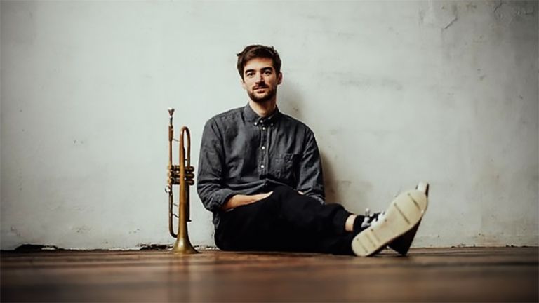 Der Musiker sitzt an eine Wand gelehnt auf dem Boden und neben ihm steht eine Trompete.