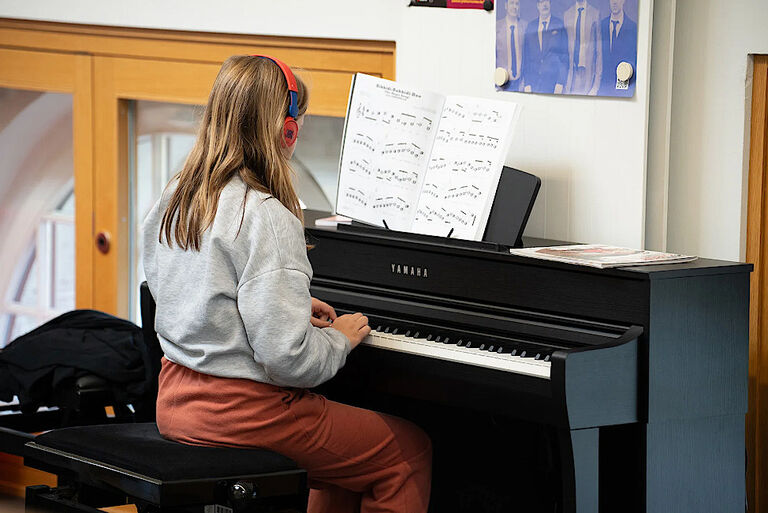 Ein Mädchen sitzt mit Kopfhörern an einm E-Piano und spielt nach Noten.