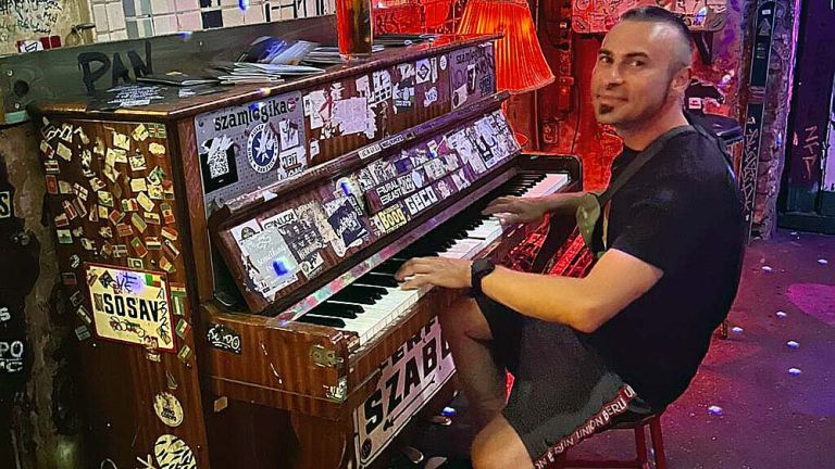 Der Musiker spielt an einem Klavier, das ganz mit Aufklebern bedeckt ist.