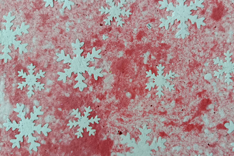 Auf blasrosa Papier sind Schneesterne zu sehen.
