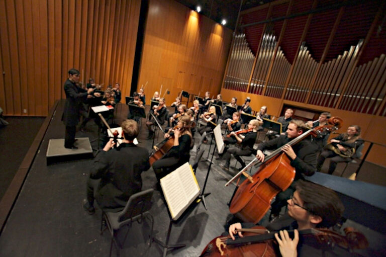 Ein Orchester spielt in einem holzvertäfelten Saal mit einer Orgel im Hintergrund