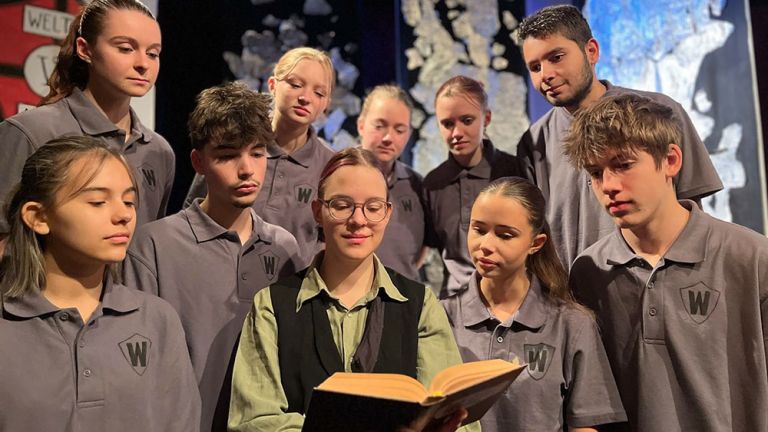 Eine Gruppe junger Schauspielerinnen und Schauspieler stellen auf der Bühne eine Schulklasse dar.