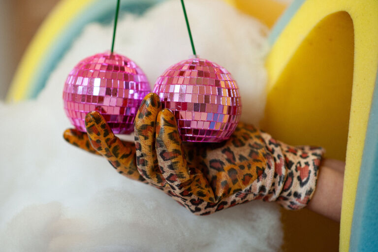 Eine Hand im Leopardenfell-Handschuh hält zwei kleine rosa-farbene Diskokugeln.