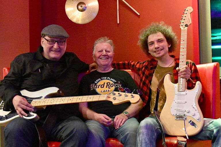 Foto der drei lachenden Musiker auf einem roten Ledersofa