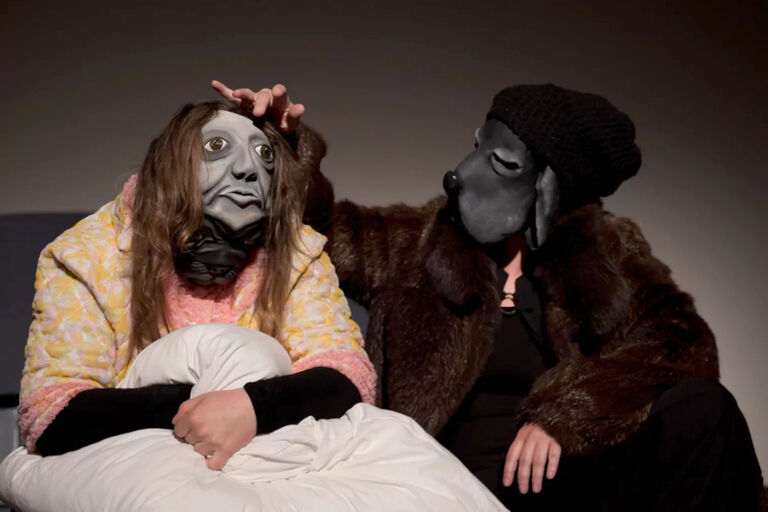 Theaterszene mit zwei Personen, die eine Maske mit einem schwermütigen Gesicht und die Maske eines Hundes tragen
