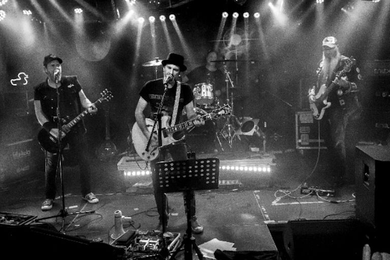 Schwarz-Weiß-Foto der Band bei einem Auftritt auf einer kleien Bühne