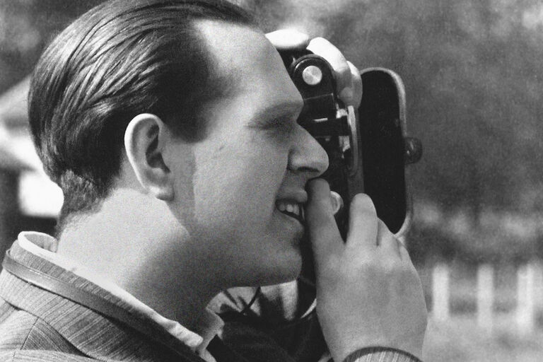 Ein historisches foto zeigt eine Nahaufnahme von Fred Stein, der durch den Sucher seiner Kamera blickt.