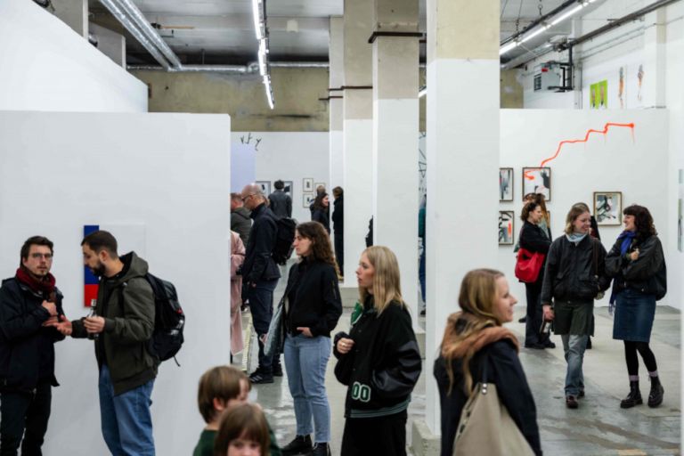In einer ehemaligen Fabrikhalle schauen sich Besucherinnen und Besucher eine Ausstellung an.