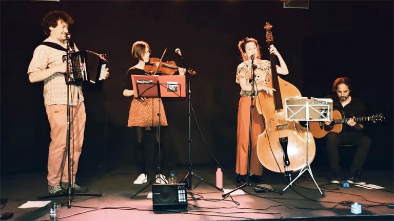 Die vier Musikerinnen und Musiker stehen bei einem Auftrit mit ihren akustischen Instrumenten nebeneinander auf der Bühne.
