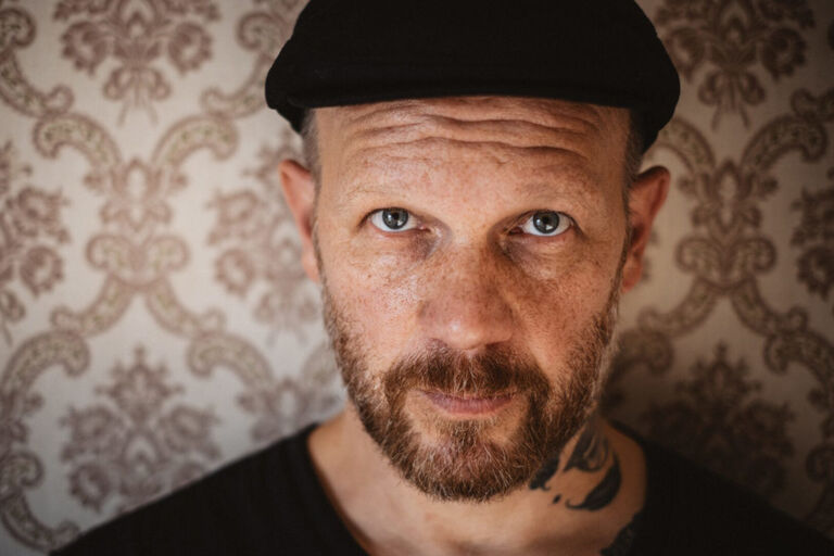 Porträtfoto des ernst blickenden Sängers vor einer altmodischen Tapete