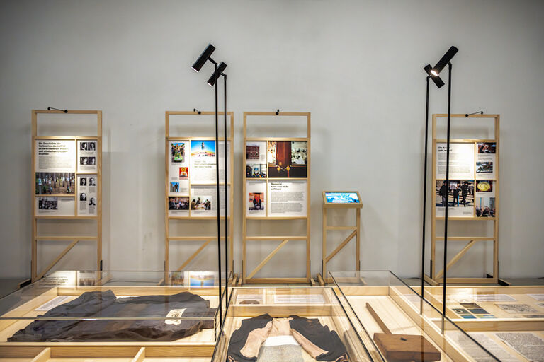 In einem Austellungsraum befinden sich Aufteller aus Holz mit Texten und fotos sowie Vitrinen mit Exponaten.