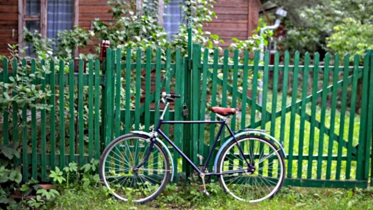 Ein Fahrrad lehnt an einem grün gestrichenen Gartenzaun.