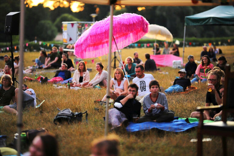 Viele Menschen sitzen oder liegen auf einer Wiese und lauschen dem Hörspielptogramm