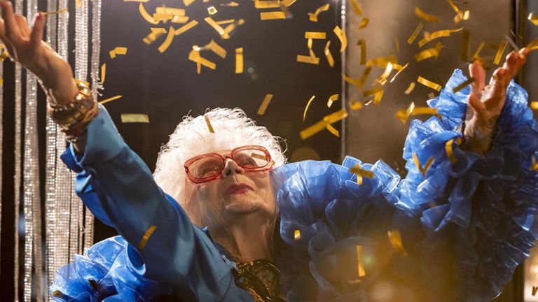 Filmszene, in der Vika mit weißen Haaren und extravagantem Outfit goldene Schnipsel in die Luft wirft.