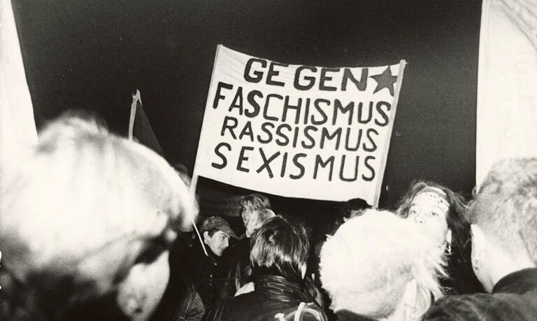 Auf einem historischen Foto tragen Jugendliche ein Transparent mit der Aufschrift: Gegen Faschismus Rassismus Sexismus.