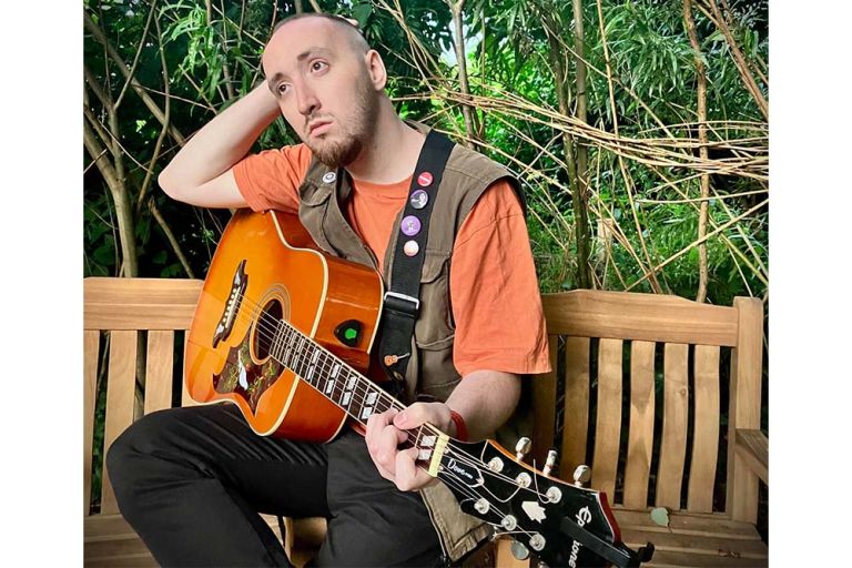 Der Musiker sitzt mit seiner Gitarre und nachdenklichem Gesicht auf einer Gartenbank.