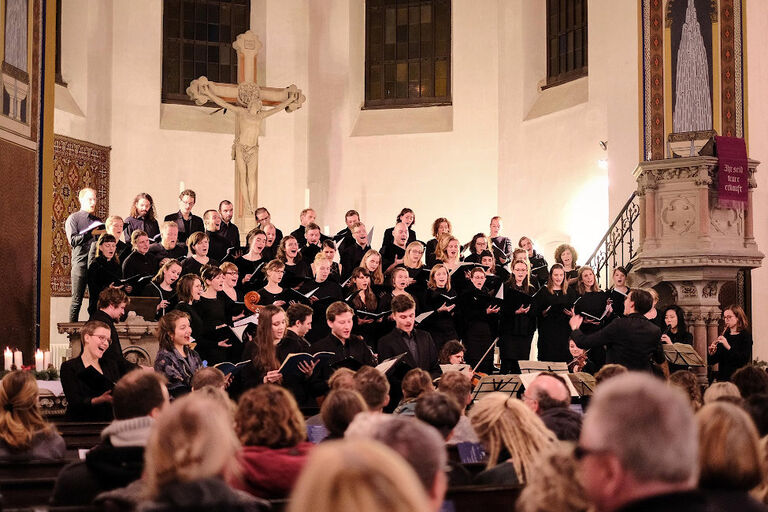 Ein Chor in schwarzer Auftrittskleidung singt in einer vollbesetzten Kirche.