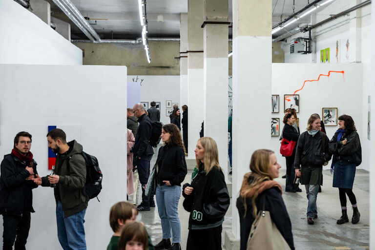 In einer großen Ausstellungshalle mit Bildern an weißen Wänden sind viele Menschen zu sehen.