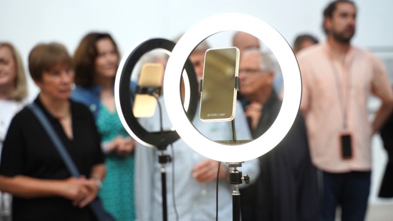 Hinter der Skulptur mit zwei Smatphones in zwei Kreisen stehen Personen, die sich unterhalten.