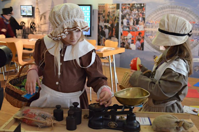 Zwei Kinder in historischen Trachten spielen mit einer alten Waage im Museum.