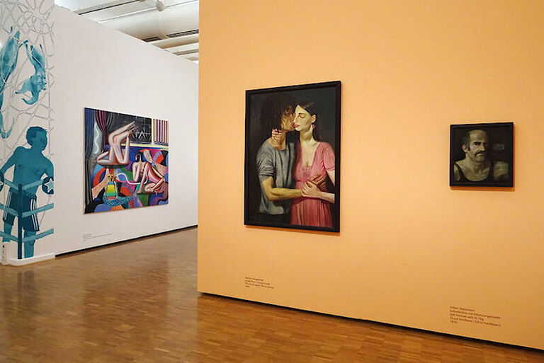 Blick in die Ausstellung, in der Gemälde in unterschiedlichen Größen an weißen und orangenen Wänden hängen