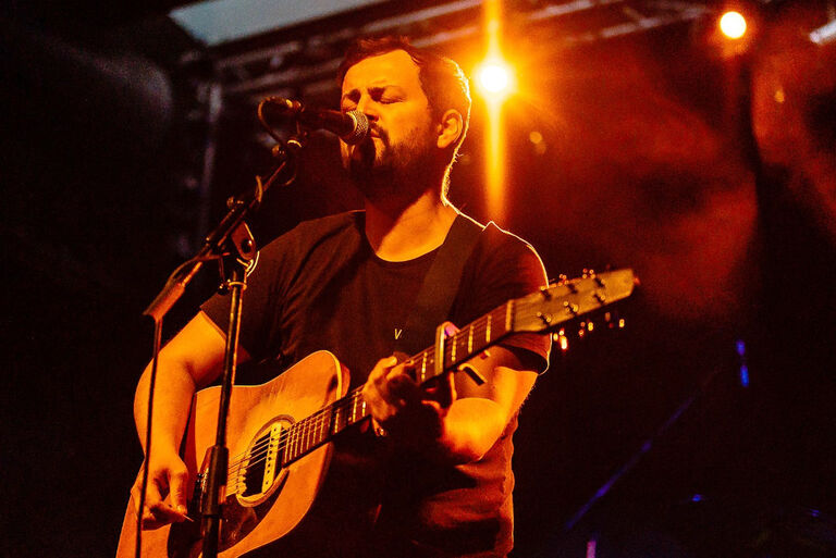 Der Sänger bei einem Auftritt mit Gitarre vor einem Mikrofon