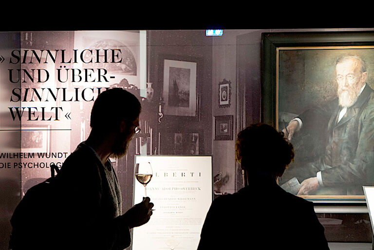 Besucher stehen vor einer Vitrine mit Bildern und Schriftstücken von Wilhelm Wundt.