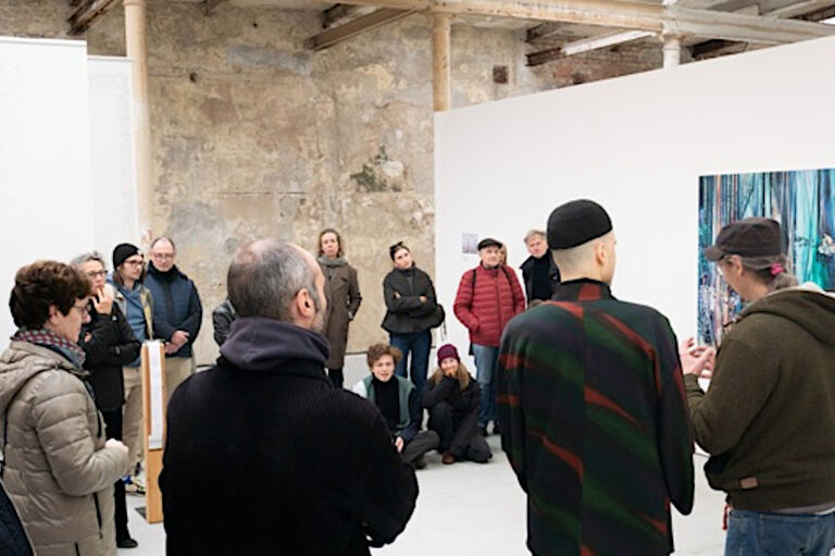 In einer Ausstellung verfolgen Besucherinnen und Besucher ein Künstlergespräch