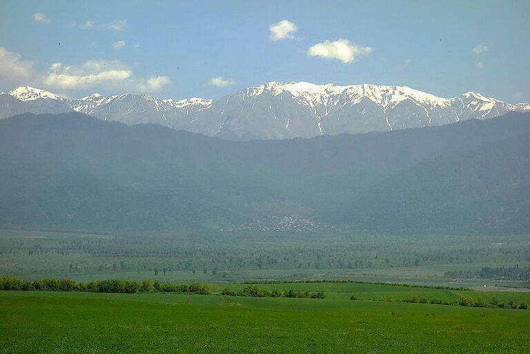 Eine weite Graslandschaft reicht bis zu einer Hügelkette, hinter der die schneebedeckten Gipfel des Kaukasus zu sehen sind.