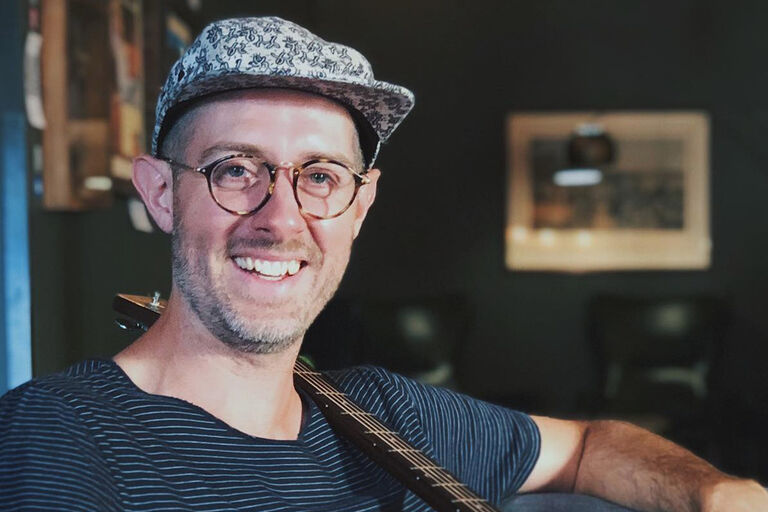 Nahaufnahme des freundlich lächlnden Künstlers mit seiner Gitarre über der Schulter