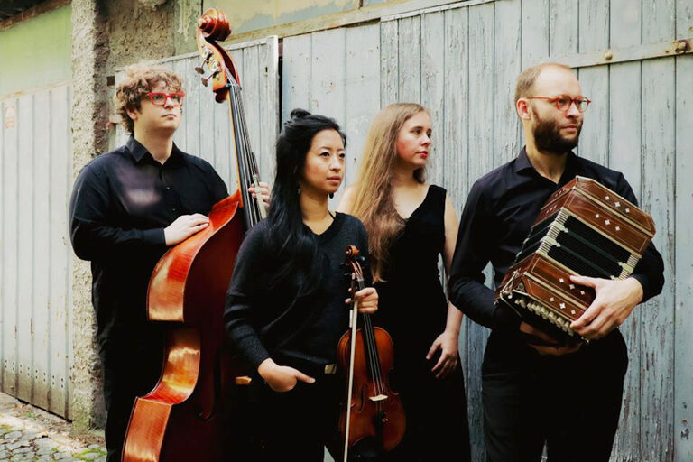 Gruppenfoto des Quartetts mit seinen Instrumenten vor einer Bretterwand