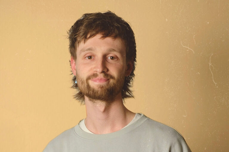 Portraitfoto des jungen Musikers mit Vollbart, der freundlich in die Kamera lächelt