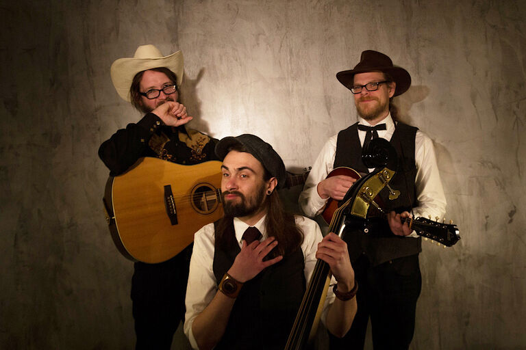 Gruppenfoto des verschmitzt blickenden Trios in Westernkleidung