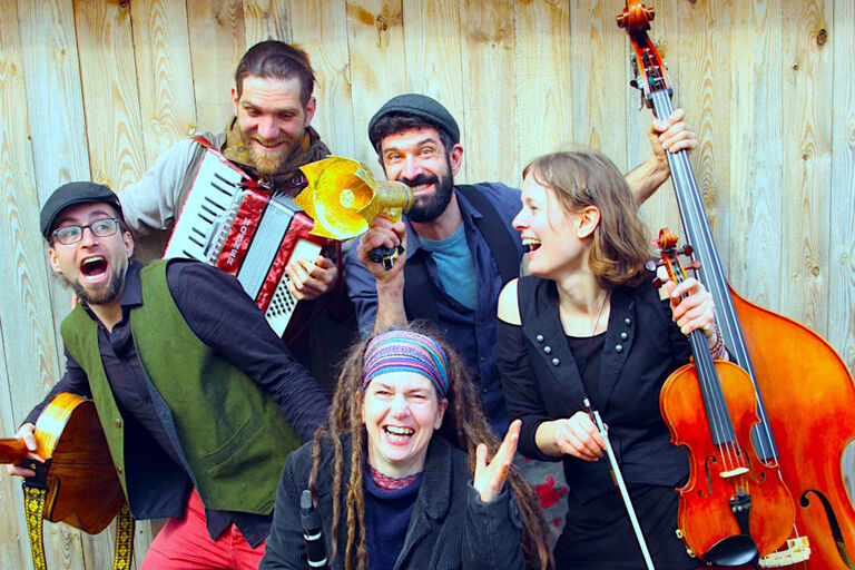 Fröhliches Gruppenfoto der Band mit ihren Instrumenten vor einer Bretterwand