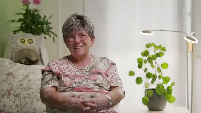 Eine Protagonistin des Films sitzt auf dem Sofa in ihrer liebevoll gestalteten Wohnung und lächelt in die Kamera