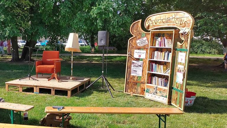 In einem kleinen Park stehen Bänke, ein Bücherschrank und ein Podium mit Sessel