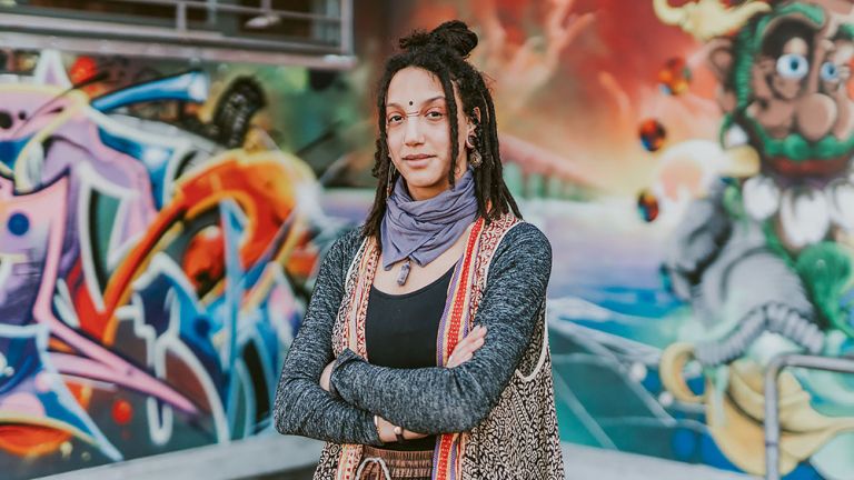 Portraitfoto der Künstlerin vor einer Wand mit farbenfrohen Grafitti