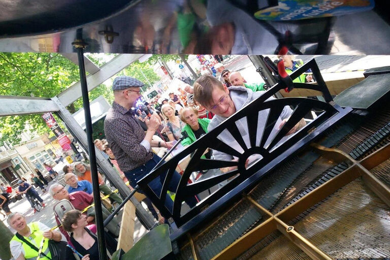 Auf der Ladefläche eines Fahrzeuges spielt ein Pianist auf einem Flügel, gefolgt von einem Protestzug.