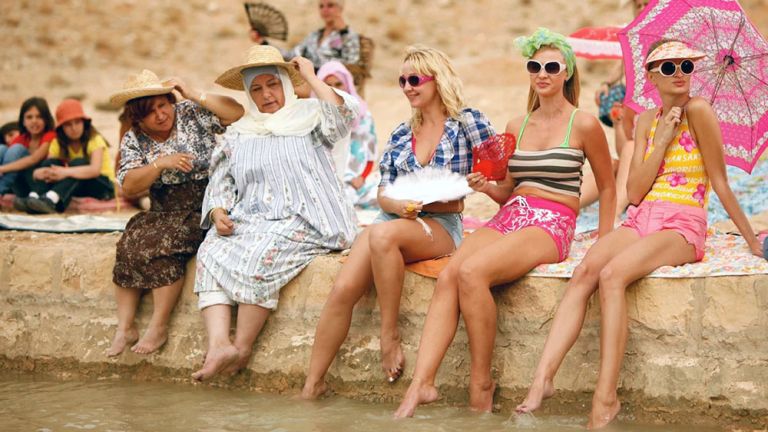 Frauen in sommerlicher westlicher Kleidung und Frauen in traditioneller arabische Kleidung sitzen nebeneinander an einem Kanal und halten ihre nackten Füße ins Wasser.