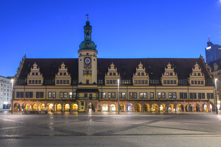 Das Alte Rathaus in Leipzig bei Nacht mit erleuchteten Fenstern und Läden im Erdgeschoss