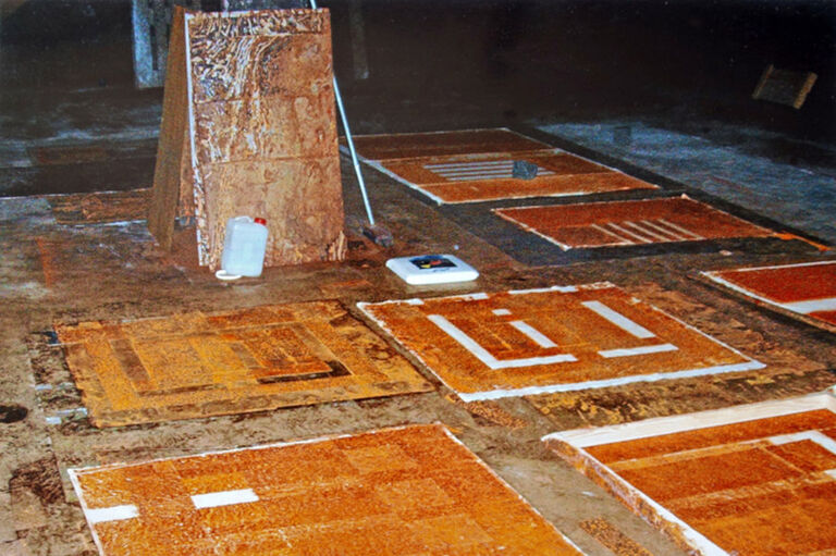In einem großen Raum sieht man rostige Metallplatten und Materialien, auf die der Rost übertragen wurde.